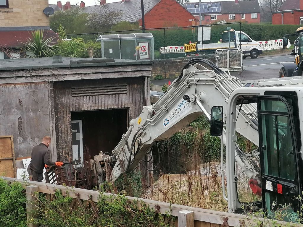 Digger demolishing an old overgrown classroom.