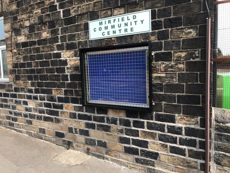 Sandstone wall with a sign saying Mirfield Community Centre above a new noticeboard. 